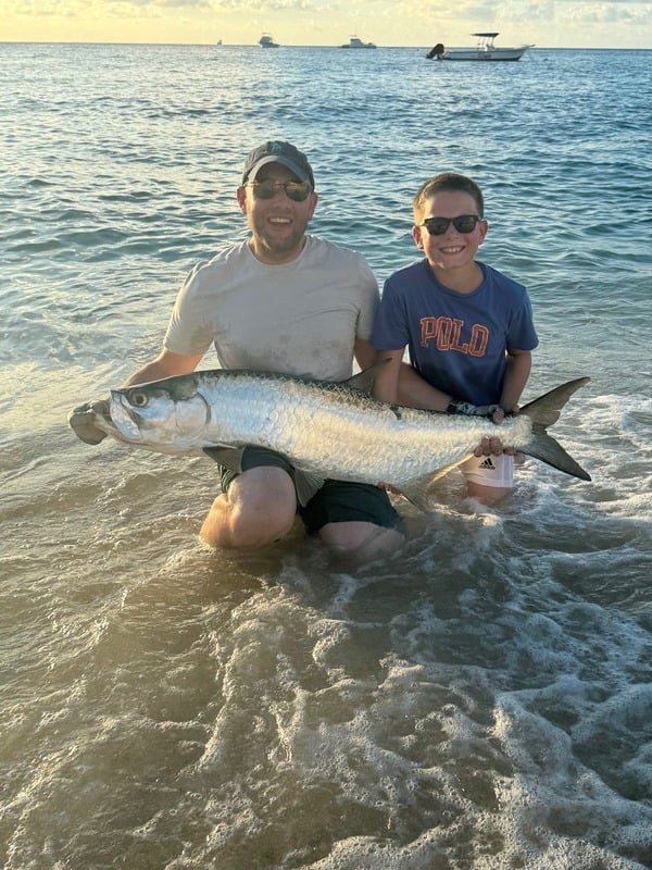 Father and son holding a large tarpon caught from shore at sunset in Grand Cayman, Cayman Islands
