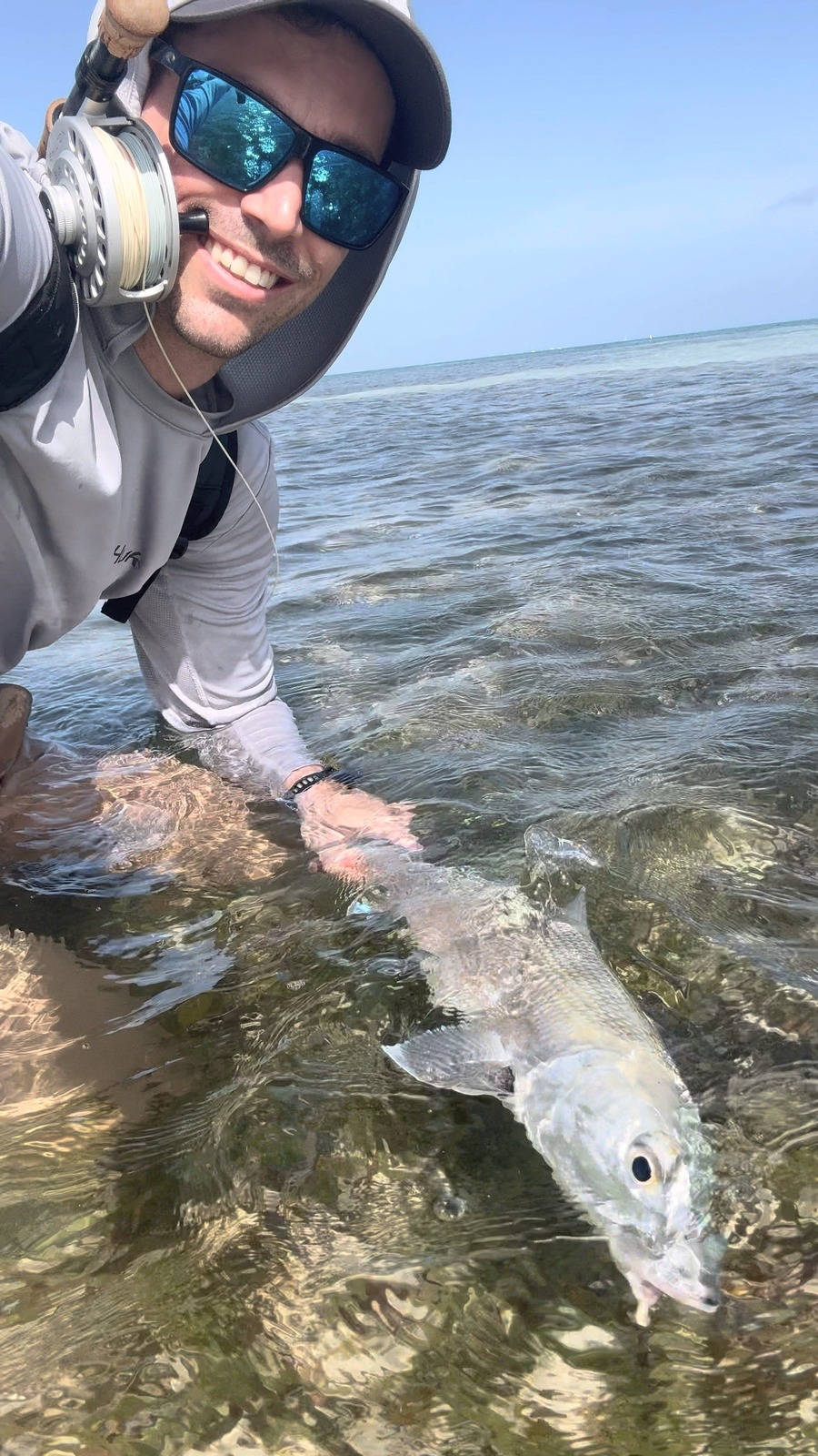 Smiling fly angler releasing a bonefish caught on fly on a clear shallow flat in Grand Cayman, Cayman Islands